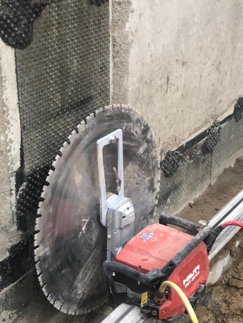 Wandsäge mit großem Sägeblatt schneidet senkrecht durch Betonwand mit Schutzfolie