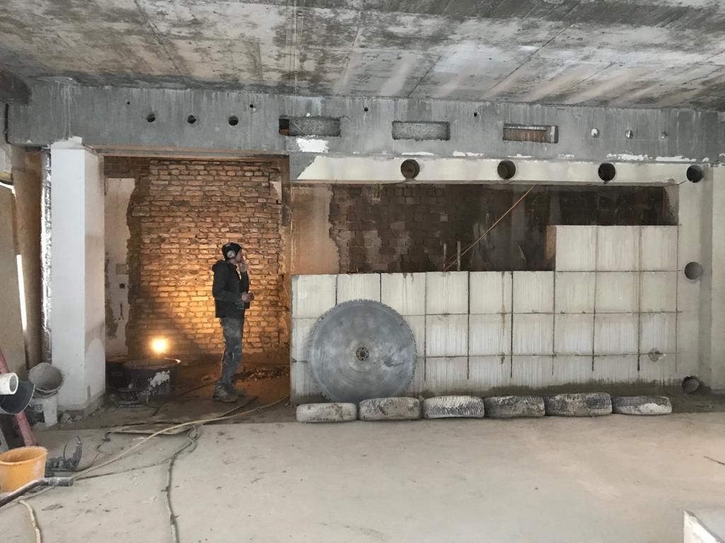 Mitarbeiter in Schutzkleidung bei Wanddurchbruch, große Betonsäge und Bohrkerne im Vordergrund